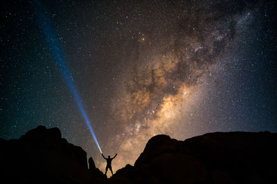 Low angle view of silhouette man standing on mountain against star field