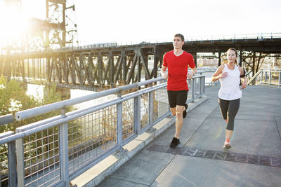 Friends jogging together on bridge against clear sky