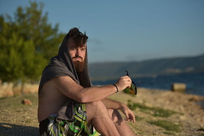 Portrait of bearded man sitting at beach against sky