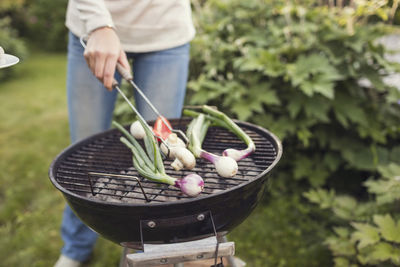 Midsection of teenage girl cooking vegetable on barbecue grill in back yard