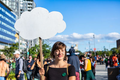 Portrait of smiling young woman in city against sky