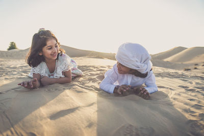 Siblings lying at desert against sky