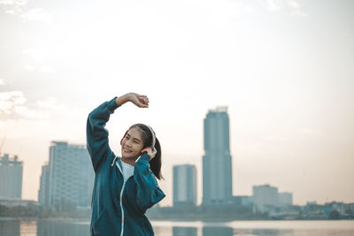 Full length of happy woman standing against buildings in city