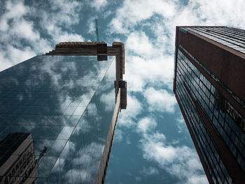 Low angle view of modern glass buildings against cloudy sky