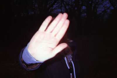 Cropped image of person hand against tree at night