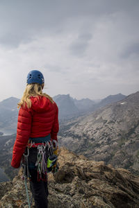 Female hiker with mountain climbing equipment looking at view while standing on cliff against sky