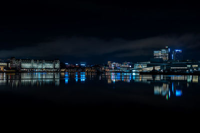 Illuminated buildings by river against sky at night