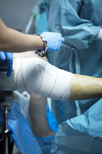 Midsection of surgeon wrapping adhesive bandage on patient leg in hospital