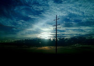 Electricity pylon on field against cloudy sky