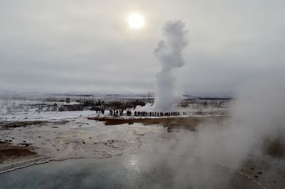 People at strokkur geyser erupting against sky
