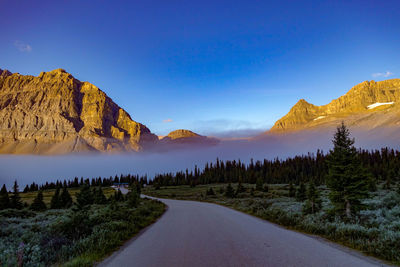 Scenic view of road by mountains against blue sky