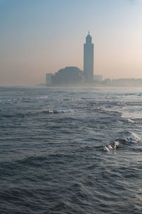 Lighthouse by sea against sky during sunset