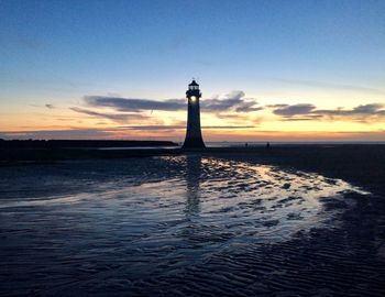 Lighthouse by sea against sky during sunset