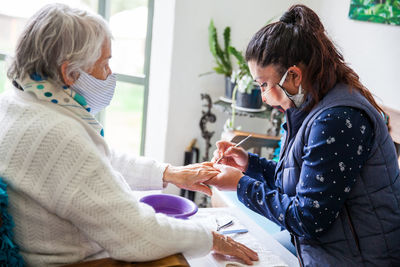 Woman wearing mask doing manicure of customer at home