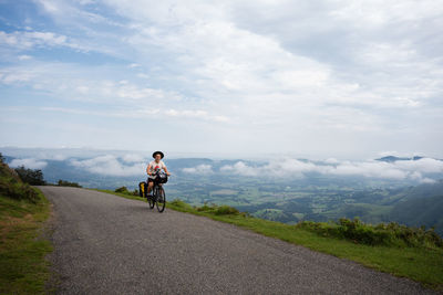 Rear view of man riding bicycle on road against sky