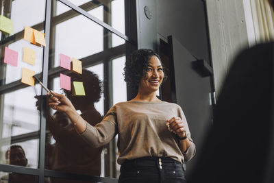 Happy mature businesswoman explaining adhesive notes in creative office