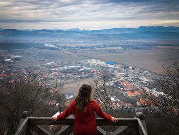 Rear view of young woman in red sweater looking down at the city from the top of a hill