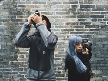 Young woman using phone while standing on brick wall