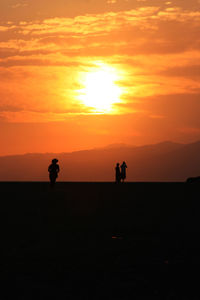 Silhouette people standing on landscape against orange sky during sunset