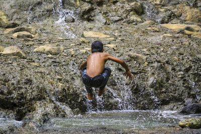 Rear view of shirtless man jumping from rock by river