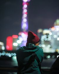 Rear view of man standing at illuminated city at night