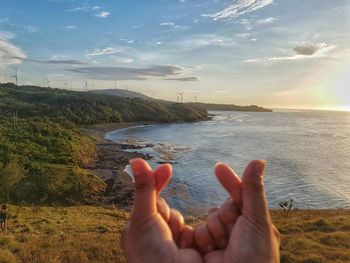 Midsection of person hand by sea against sky