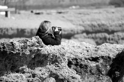 Side view of woman photographing amidst rocks at shore