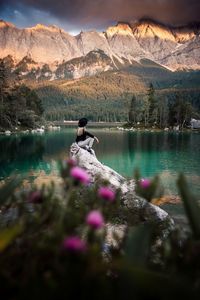 Woman sitting on rock by lake against mountains and sky