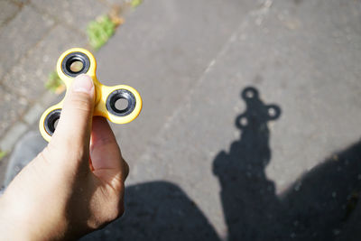 Cropped image of hand holding yellow fidget spinner over road on sunny day