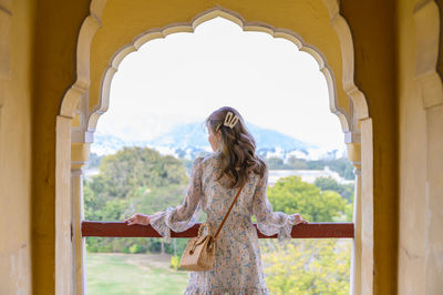 Rear view of woman standing at balcony seen through arch