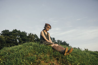 Woman sitting on a hill in a dress and boots