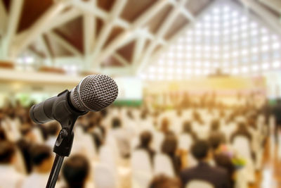 Close-up of microphone with people sitting on chairs