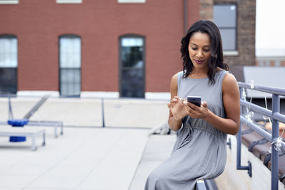 Businesswoman using smart phone while sitting railing at building terrace