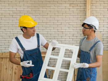 Young man with woman wearing hat standing against brick wall