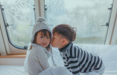 Brother kissing sister on bed at home