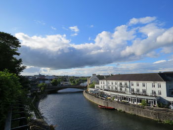 Bridge over river by buildings in city against sky