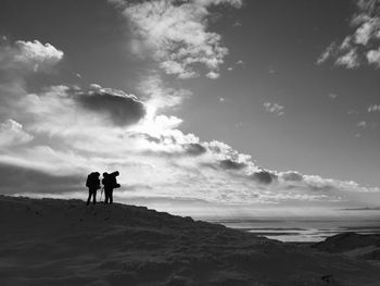 Silhouette men standing on shore against sky