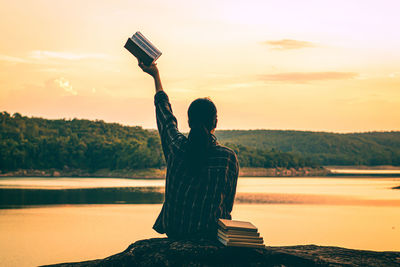 Rear view of woman standing by lake against sky during sunset