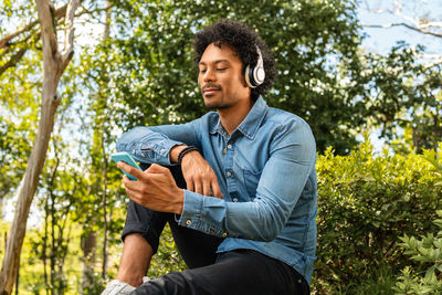 Young man looking away while sitting on tree