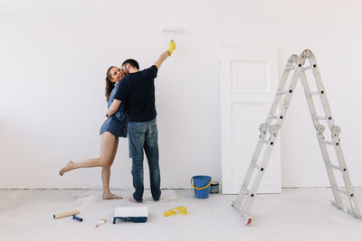 A young couple in love have moved into a new house and are making repairs painting white walls