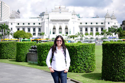 Portrait of smiling woman walking on footpath against historical building