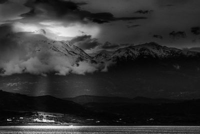 Scenic view of sea and mountains against storm clouds