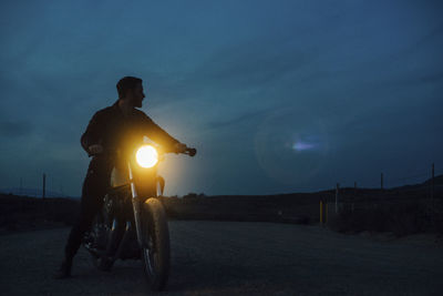 Low angle view of man riding illuminated motorcycle on street at dusk