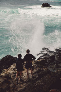 Rear view of men standing on rock in sea