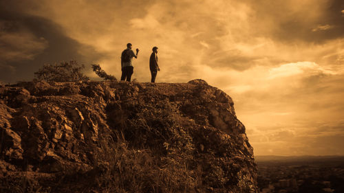 People standing on cliff against sky during sunset