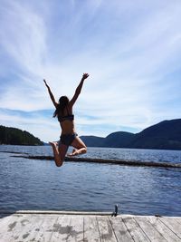 Full length rear view of woman jumping in lake against mountains and sky