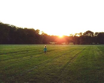 People on grassy field against clear sky during sunset