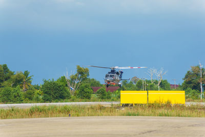 Yellow airplane flying over field against sky