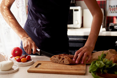 Woman is cutting a french fresh crispy baguette in the kitchen. basil, tomatoes and mozzarella 