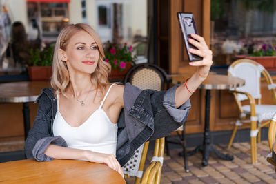 Young cute woman using phone sits in cafe at table with smartphone, answering person